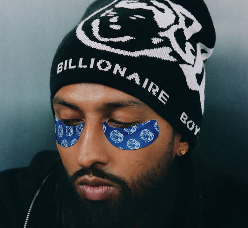 Brightening undereye patches from Topicals worn by a bearded man in a Billionaire Boys Club beanie with eyes closed.